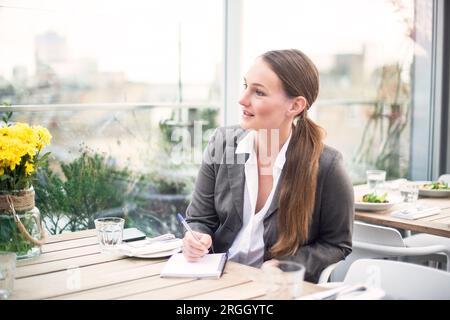 Giovane imprenditrice iscritto su appunti ad una riunione in un ristorante Foto Stock