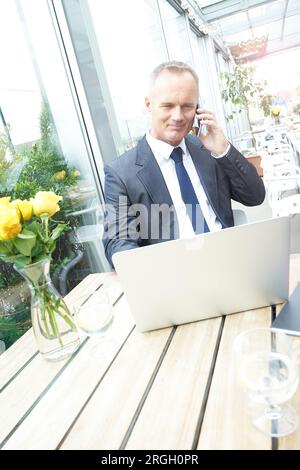 Imprenditore utilizza lo smartphone e il computer portatile in ristorante Foto Stock