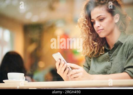 Giovane donna utilizzando smart phone dietro la finestra cafe Foto Stock
