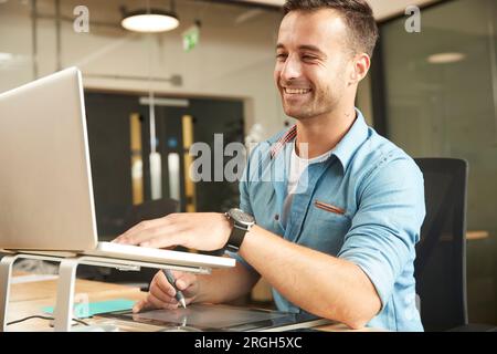Sorridente giovane uomo che lavora sul computer portatile Foto Stock
