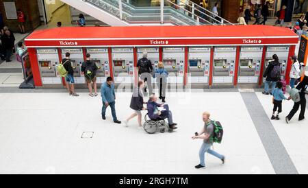 Fila automatizzata di distributori automatici di biglietti all'interno della stazione di Liverpool Street persone viaggiatori turisti che camminano lungo l'atrio con borse per bagagli Londra Regno Unito Foto Stock