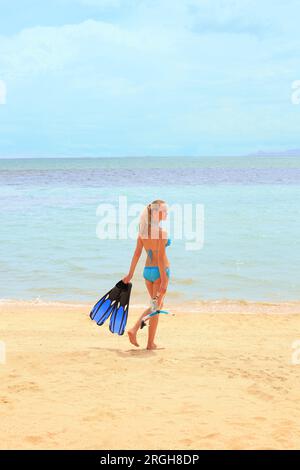 Giovane donna che indossa un bikini azienda pinne sulla spiaggia Foto Stock