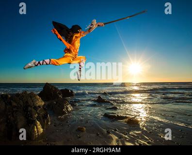 Giovane donna con la spada jumping in arti marziali uniforme sulla spiaggia Foto Stock