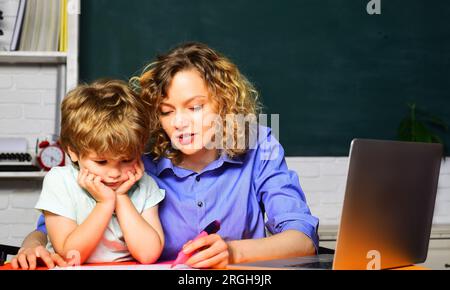 Insegnante che aiuta i bambini della scuola elementare in classe a fare i compiti. Conoscenza, studio, istruzione e apprendimento. Piccolo bambino alle elementari Foto Stock