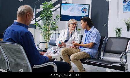 Specialista senior per la misurazione del livello di insulina e del glucosio nel campione di sangue utilizzando uno strumento glucometro, consultando un paziente asiatico. Medico che fa un test medico durante l'esame in accoglienza ospedaliera Foto Stock