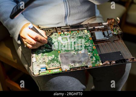 riparazioni di computer, anziana donna degli anni settanta che ripara il suo notebook, tenendo la luce del telefono per vedere meglio Foto Stock