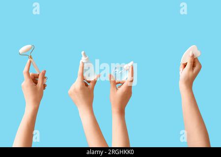 Donna con strumenti per massaggi e biberon con contagocce cosmetico su sfondo blu Foto Stock