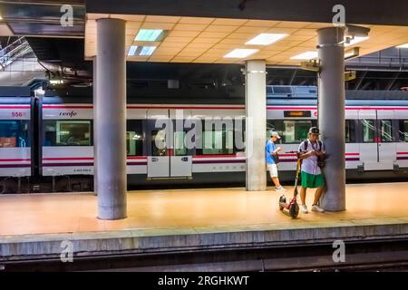 Due uomini, uno con uno scooter, sul binario in attesa dell'arrivo del loro treno alla stazione ferroviaria di Atocha Cercanias a Madrid in Spagna. Foto Stock