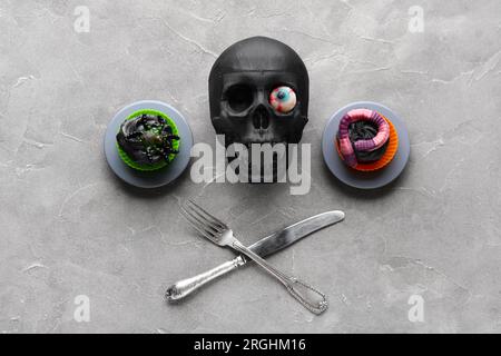 Composizione con teschio, posate e deliziosi cupcake di Halloween su sfondo grigio Foto Stock