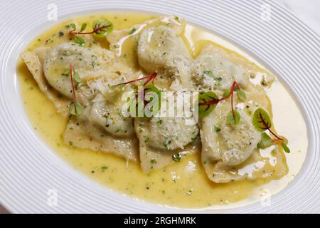 Piatti italiani, ravioli ripieni di funghi con salsa cremosa di parmigiano in un piatto bianco Foto Stock