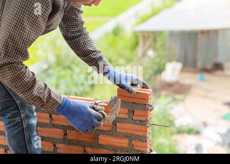 Mano ravvicinata della mansoneria per l'installazione di mattoni di calcestruzzo per pareti di edifici in cantiere. Foto Stock