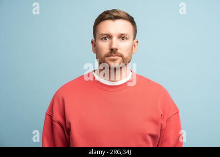 Un uomo triste e preoccupato, con un'espressione facciale seria, guarda la fotocamera su sfondo blu in studio Foto Stock