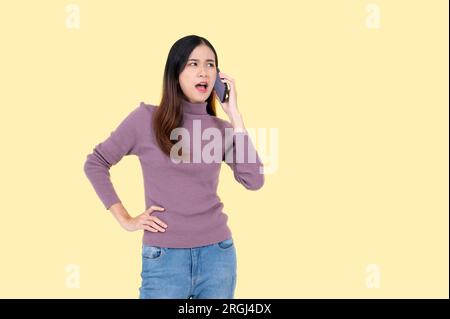 Una donna asiatica insoddisfatta e infelice sta parlando al telefono in modo aggressivo, lamentandosi di qualcuno al telefono, sentendosi insoddisfatta. isolato y Foto Stock