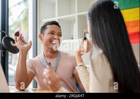 Un podcaster gay asiatico attraente e gioioso, o conduttore radiofonico, è stato inventato da una makeup artist femminile nel suo studio. Stile di vita LGBT, Moda e B. Foto Stock