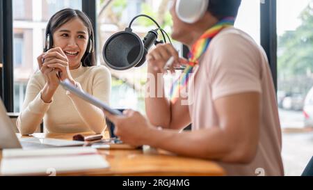 Una bellissima conduttrice radiofonica asiatica di podcast ama parlare con il suo collega gay mentre registra un podcast in studio. Foto Stock