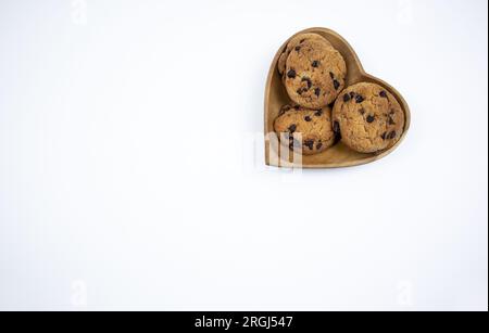 Biscotti con gocce di cioccolato su un piatto a forma di cuore su sfondo bianco Foto Stock