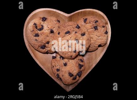 Biscotti con gocce di cioccolato su un piatto a forma di cuore su sfondo nero Foto Stock