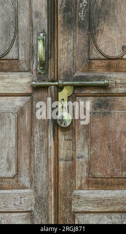 primo piano di una maniglia scorrevole in metallo vecchio stile e di un bullone con serratura su una classica porta in legno vintage Foto Stock
