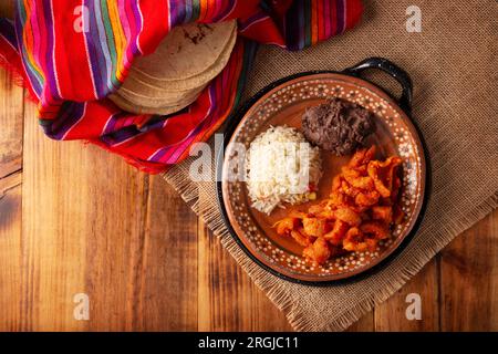 Chicharron en salsa roja. Croste di maiale stufate in salsa rossa accompagnate da riso e fagioli fritti. Piatto tradizionale fatto in casa molto popolare in Messico, questo Foto Stock