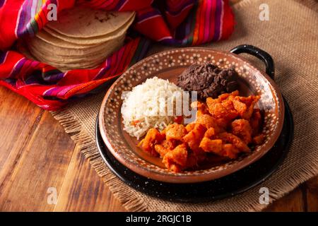 Chicharron en salsa roja. Croste di maiale stufate in salsa rossa accompagnate da riso e fagioli fritti. Piatto tradizionale fatto in casa molto popolare in Messico, questo Foto Stock