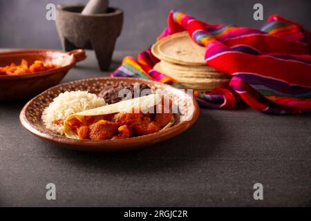 Chicharron en salsa roja. Croste di maiale stufate in salsa rossa accompagnate da riso e fagioli fritti. Piatto tradizionale fatto in casa molto popolare in Messico, questo Foto Stock