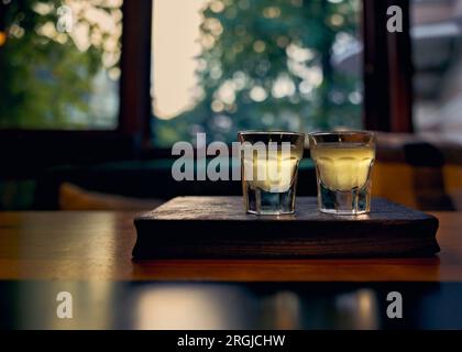 Due bicchieri con limoncello su un cavalletto di legno sullo sfondo di una finestra blu Foto Stock