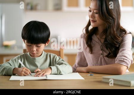 giovane madre asiatica seduta al tavolo a casa che aiuta il figlio con il suo studio Foto Stock