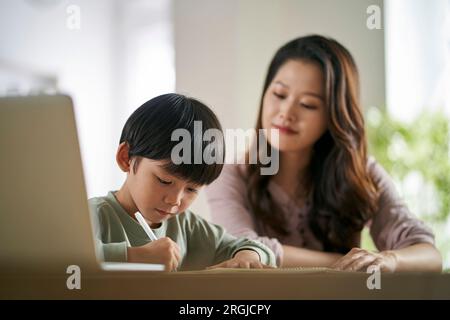 giovane madre asiatica seduta al tavolo a casa che aiuta il figlio con il suo studio Foto Stock