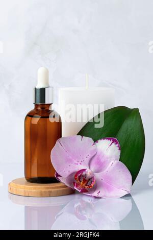 Primo piano della bottiglia di siero in vetro marrone e della candela bianca profumata in bagno. Essenza, olio per massaggi. Fiore d'orchidea. Prodotti di bellezza naturali biologici del centro benessere Foto Stock