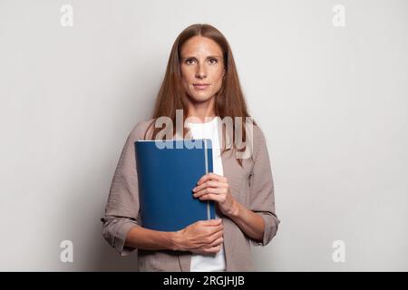 Una donna d'affari seria e sicura di successo tiene una cartella con un rapporto annuale o documenti su sfondo bianco Foto Stock