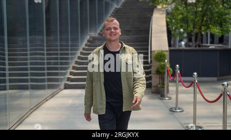 Joyful caucasian Guy passa davanti a un edificio commerciale. Foto Stock