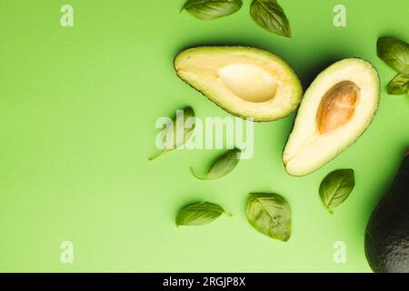 Primo piano di due metà di foglie di avocado e basilico e spazio di copia su sfondo verde Foto Stock