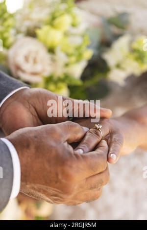 Mani dello sposo birazziale senior che mettono l'anello nuziale al dito della sua sposa Foto Stock