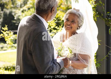 Felice sposo e sposo birazziale durante la cerimonia nuziale nel giardino soleggiato Foto Stock