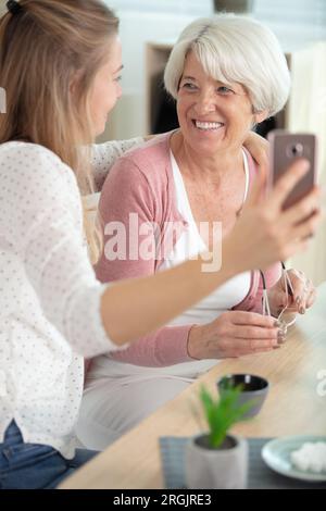 la madre anziana siede sul divano con una figlia adulta che tiene lo smartphone Foto Stock