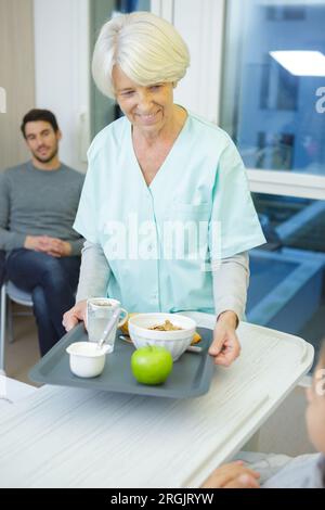 infermiera anziana che tiene un vassoio per la colazione per bambini Foto Stock