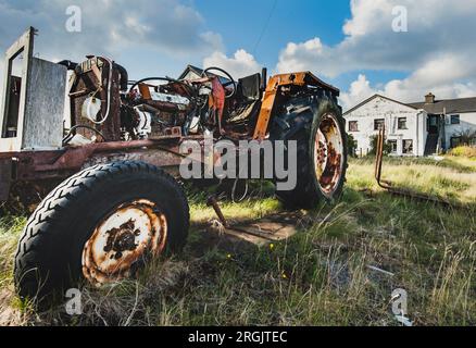 Trattore vecchio con parti della carrozzeria mancanti, poiché il motore arrugginito e le parti meccaniche sono visibili. Un veicolo agricolo abbandonato porta al declino della coltivazione Foto Stock