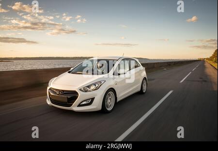 White Hyundai i30 in auto lungo un enorme lago. Ripresa in movimento di una berlina compatta coreana in un ambiente rurale. Foto Stock
