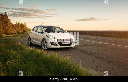 Hyundai i30 bianca parcheggiata lungo la strada, erba verde in primo piano. Berlina compatta coreana in ambiente rurale. Foto Stock