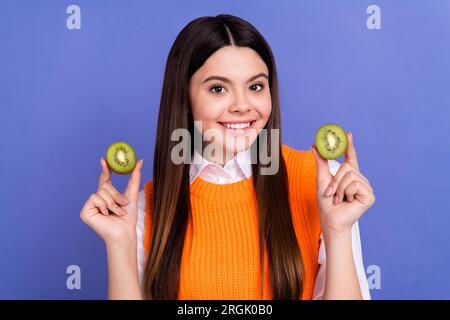 Foto di adorabile ragazza positiva che trasmette le mani del sorriso reggono due metà kiwi isolate su sfondo di colore viola Foto Stock