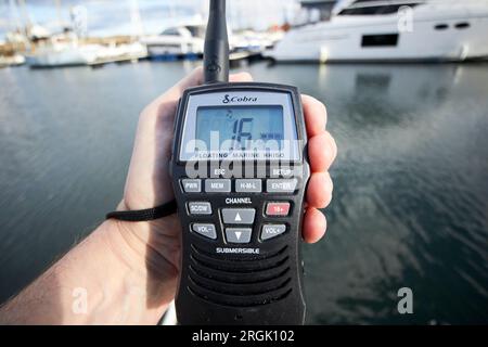 uomo in possesso di radio vhf portatile di emergenza cobra sintonizzato sul canale 16 su una piccola barca in un porticciolo nel regno unito Foto Stock