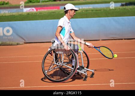 L'uomo pratica tennis su una sedia a rotelle su un campo in terra battuta. Tennis su sedia a rotelle. Foto Stock