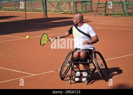 L'uomo pratica tennis su una sedia a rotelle su un campo in terra battuta. Tennis su sedia a rotelle. Foto Stock