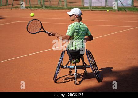 L'uomo pratica tennis su una sedia a rotelle su un campo in terra battuta. Tennis su sedia a rotelle. Foto Stock