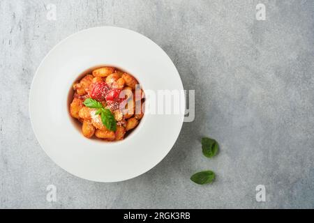 Gnocchi di patate. Gnocchi di patate tradizionali fatti in casa con salsa di pomodoro, basilico e parmigiano sul tavolo da cucina grigio chiaro backgrou Foto Stock