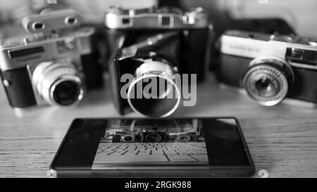 Immagine in bianco e nero di tre fotocamere d'epoca insieme a un moderno telefono con fotocamera, che illustano il vecchio e il nuovo. Foto Stock