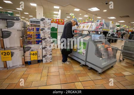 Uomo anziano che guarda le prime pagine dei giornali britannici mentre si trova in un supermercato, Londra, Inghilterra, Regno Unito Foto Stock