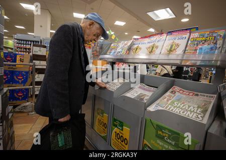 Uomo anziano che guarda le prime pagine dei giornali britannici mentre si trova in un supermercato, Londra, Inghilterra, Regno Unito Foto Stock