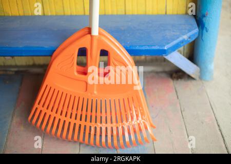 Scopa arancione. Strumento di pulizia. Strumento giardino. Setole in plastica per la raccolta di scarichi a secco. Foto Stock