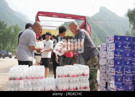 Baoding, provincia cinese di Hebei. 10 agosto 2023. Gli abitanti del villaggio scaricano cibo e acqua in bottiglia da un camion nella Longmen Township della contea di Laishui, nella provincia di Hebei nella Cina settentrionale, 10 agosto 2023. Colpiti da forti piogge, alcuni villaggi della contea di Laishui hanno incontrato interruzioni del traffico e delle comunicazioni. Le autorità locali hanno fatto tutto il possibile per riparare le infrastrutture danneggiate dalle inondazioni, fornendo al contempo forniture di soccorso acquistate dal governo e donate da tutti i ceti sociali ai residenti colpiti dalle inondazioni. Crediti: Yang Shiyao/Xinhua/Alamy Live News Foto Stock